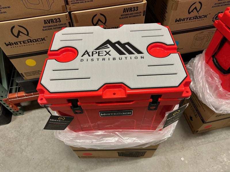 Load image into Gallery viewer, Red WhiteRock rotomolded cooler with Apex Distribution logo on the gray lid, in warehouse setting
