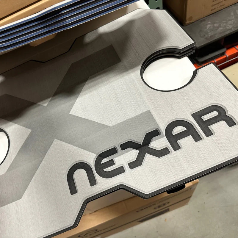 Load image into Gallery viewer, Close-up of stacked custom cut metal plates with Nexar logo in a warehouse
